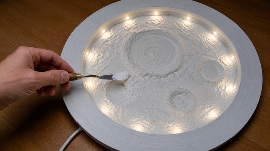 Strukturpaste wird mit einem Spachtelmesser auf eine leuchtende Mondlampe im Workshop der Einzigmacherei Norderstedt aufgetragen.